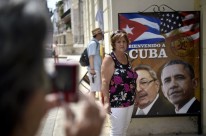 Cubana posa para uma foto ao lado de um cartaz que mostra as imagens de Castro e Obama; é grande a expectativa pela visita