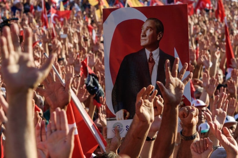 Demonstrators rise their hands and hold a potrait picture of Mustafa Kemal Ataturk, founder of modern Turkey, as they gather at Taksim Square in Istanbul on July 24, 2016. Many thousands of flag-waving Turks massed on July 24, 2016, for the first cross-party rally to condemn the coup attempt against President Recep Tayyip Erdogan, amid an ongoing purge of suspected state enemies. 