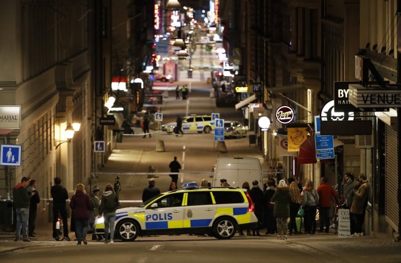 People stand behind the cordon as the police work at the scene after a truck slammed into a crowd of people outside a busy department store in central Stockholm, causing 