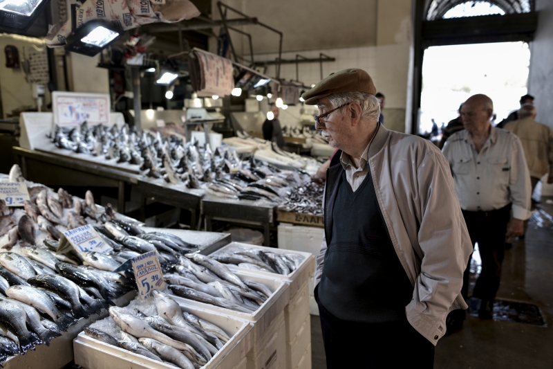 Um homem observa o preço dos peixes em um mercado de Atenas